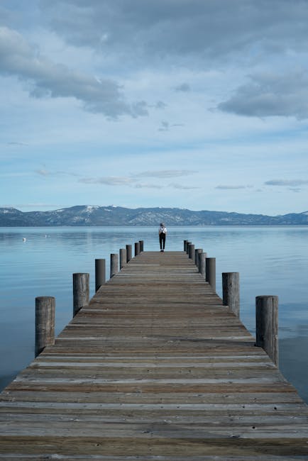 A person enjoying a moment of calm, sitting on a wooden pier by a tranquil lake at dusk
