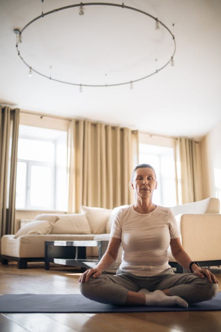 Woman peacefully doing a yoga pose on a mat in a spacious, sunlit room, with eyes closed